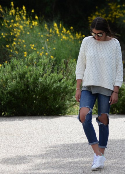 white cable knit sweater with ripped and tied blue jeans
