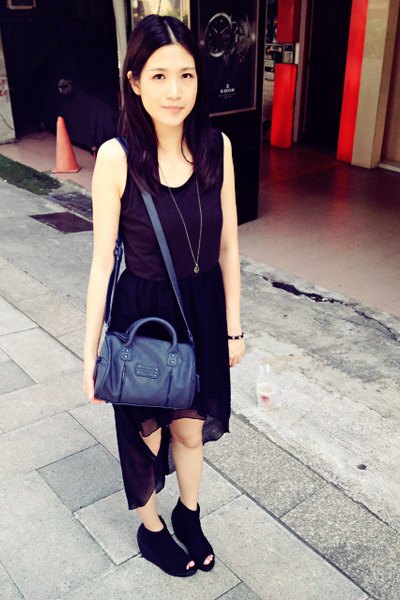 black sleeveless dress with a high chiffon and scoop neckline and a dark blue handbag
