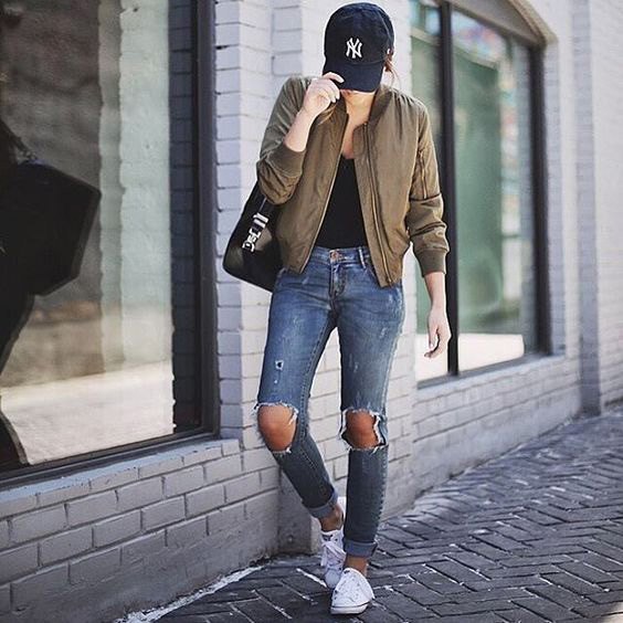 Green bomber jacket worn with a black scoop neck top and badly ripped jeans