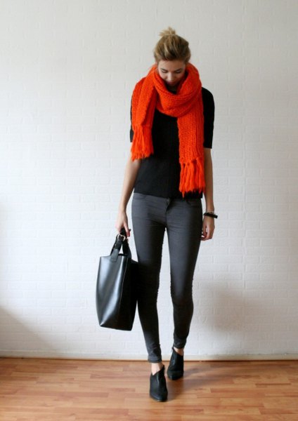 black sweater with an orange scarf with fringes and gray skinny jeans