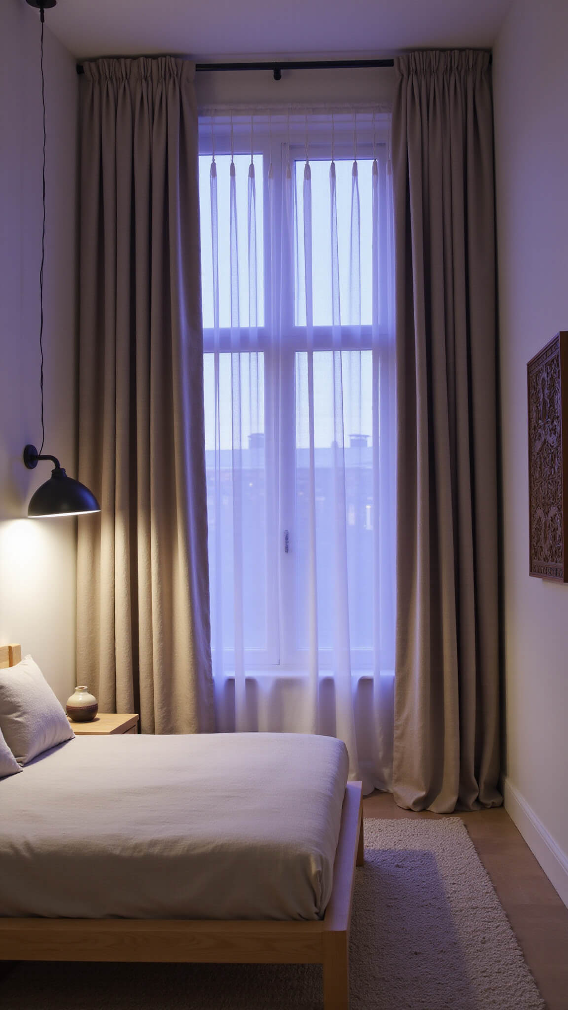 Serene bedroom with floor-to-ceiling dual-layer curtains in oatmeal linen and sheer cotton, illuminated by dusk light with purple-blue undertones, featuring a bleached oak platform bed and textured monochrome décor.