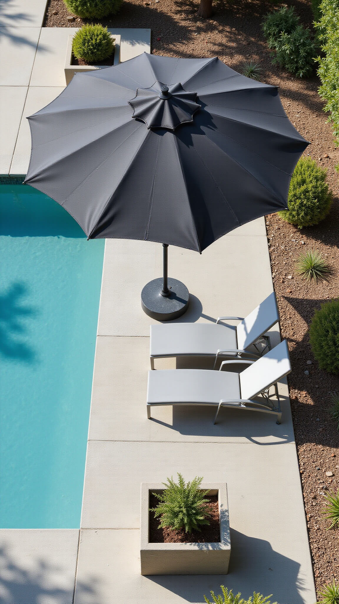 Aerial view of a modern poolside lounge featuring a large charcoal cantilever umbrella, turquoise water, sleek grey chaise lounges, and geometric succulent planters casting sharp midday shadows.