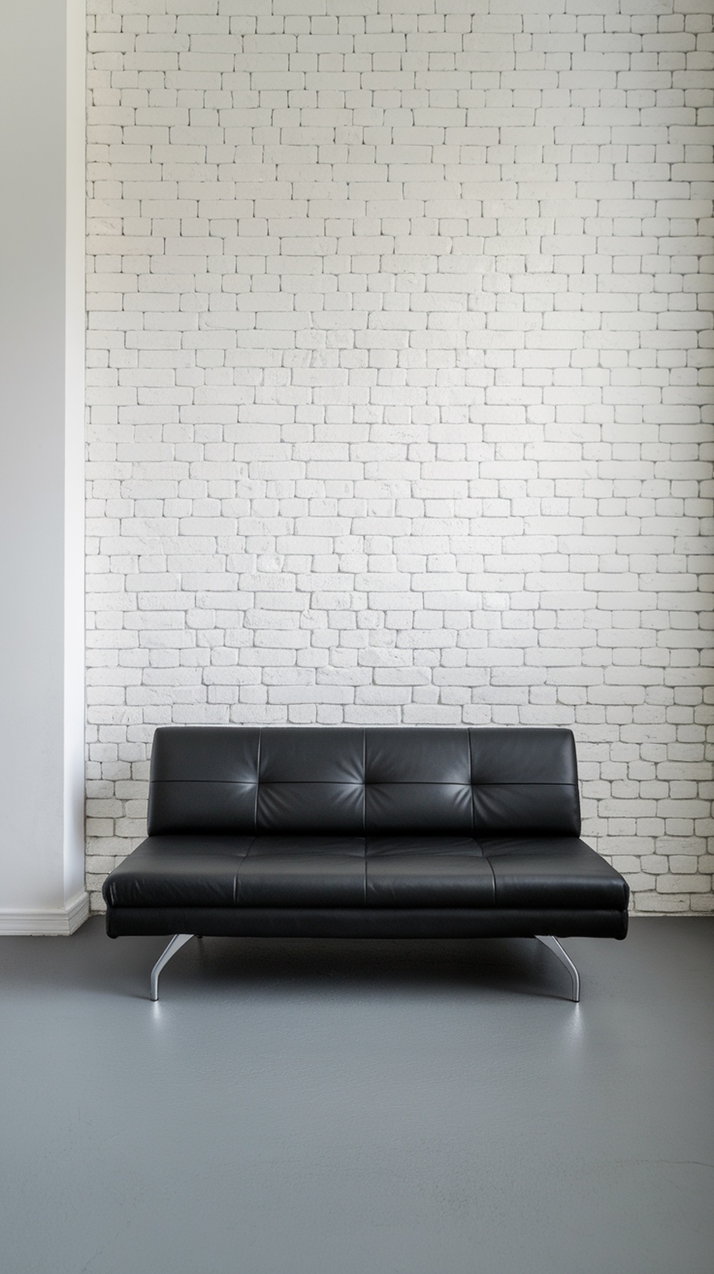 A sleek black faux leather sleeper sofa against a white brick wall in a contemporary room.